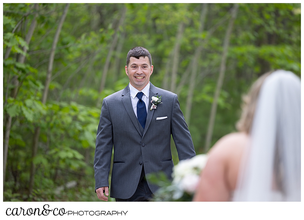 a groom wearing a gray suit, walks towards his bride, smiling broadly