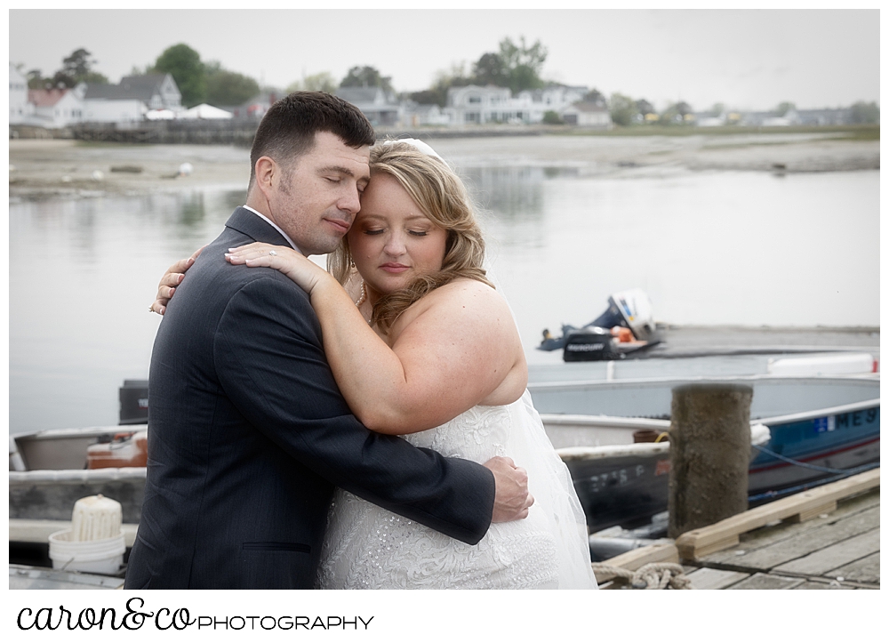 a bride and groom stand cheek to cheek on the dock at their Pine Point Maine wedding