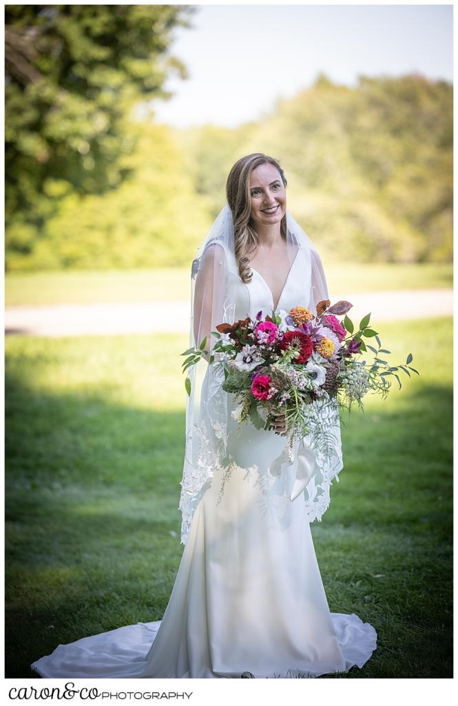 a bride in a white sleeveless wedding dress and veil, carrying a brightly colored bouquet, smiles during her Camp Skylemar wedding day first look